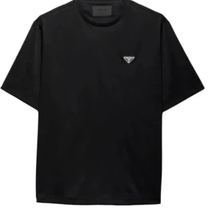 Svart t-shirt från Prada - Svart t-shirt från Prada med klassisk rund hals och korta ärmar. Diskret Prada-logga på bröstet ger en clean och lyxig vibe. Perfekt för dig som gillar stilrena och exklusiva plagg. Materialet känns mjukt och skönt mot huden.