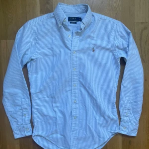Polo Ralph lauren skjorta  - Säljer dennna riktigt snygga vit och blå randiga Ralph lauren skjorta! Den är i mycket bra skick utan några defekter, storlek XS modell classic fit, den är 71 cm lång och 47 cm bred under armhålorna, hör gärna av dig vid frågor!