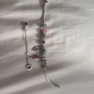 Pandora armband med berlocker - Säljer ett silverfärgat Pandora armband med flera unika berlocker. Armbandet har detaljer i rosa, rött och blått samt hjärtformade och glittriga berlocker. Några berlocker har text och motiv som hjärta, blomma och en röd solfjäder. Perfekt för dig som gillar personliga smycken. Kom privat om ni vill ha bättre bilder eller bilder på andra berlocker som inte är med på armabandet. Säljer mitt armband eftersom jag vill köpa ett i guld!!! Pris diskuteras!!! Så de kostar inte 0 kr