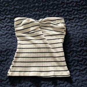 Randig bandeau tubtopp från NA-KD - Superfin bandeau tubtopp från NA-KD i ribbad bomull. Vit med mörkblå horisontella ränder och snygg twistad detalj framtill. Sitter tight och är perfekt för varma dagar. Enkel att styla med jeans eller kjol för en chill look.