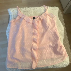 Ljusrosa prickig linnetopp med volang - Supersöt ljusrosa linnetopp från shein med små vita prickar och volangdetalj längs urringningen och framtill. Justerbara tunna axelband och lätt transparent tyg ger en luftig känsla. Perfekt för varma dagar när du vill ha en romantisk look.