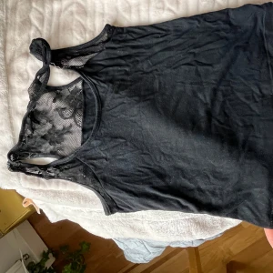 Svart linnetopp med spetsdetaljer - Säljer en svart ärmlös linnetopp med snygga spetsdetaljer och blommönster upptill och i ryggen. Toppen har rund halsringning och en tight passform som framhäver axlarna. Perfekt för dig som gillar en stilren look med en twist.