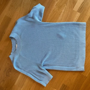 Ljusblå stickad kortärmad tröja - Snygg ljusblå stickad tröja med korta ärmar och rund hals. Tröjan har en ribbad struktur på ärmarna och runt halsen, vilket ger en cool och modern känsla. Perfekt att matcha med jeans eller kjol för en fräsch look.
