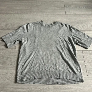 Grå stickad tröja från 157 - Snygg grå stickad tröja med lite längre i armarna och rund hals, från lager 157. Tröjan har ribbade detaljer vid hals, ärmslut och nederkant som ger en clean look. Perfekt för dig som gillar enkel och stilren design.