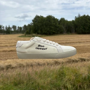 Saint Laurent skor - Snygga vita sneakers från Saint Laurent med handskriven logga på sidan. Skorna är i canvas med klassisk snörning och platt sula. Kommer med originalkartong, dustbag och äkthetskort. Perfekta för dig som gillar stilrena och exklusiva detaljer.