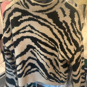 Beige och svart zebramönstrad polotröja - Säljer en beige och svart polotröja med coolt zebramönster. Tröjan är stickad och har en hög krage som ger extra stilpoäng. Perfekt för dig som vill sticka ut med ett djuriskt mönster och samtidigt hålla dig varm under hösten och vintern.