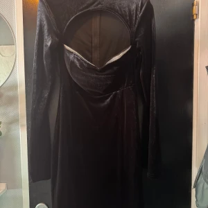 Svart sammetsklänning  - Supersnygg svart sammetsklänning med lång ärm . Klänningen har en markerad byst med glittriga detaljer längs kanten och en dragkedja bak. Perfekt för dig som vill sticka ut med en unik look och mjukt material.