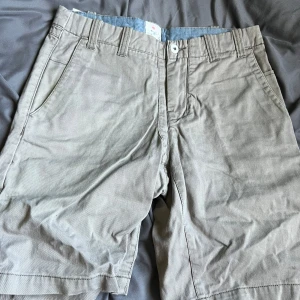 Beige bomullsshorts från Fair Compromise - Klassiska beige shorts från Fair Compromise i 100% bomull. De har normal passform, bälteshällor och sidofickor. Perfekta för varma dagar och enkla att matcha med det mesta. Snygg och stilren look som funkar till många olika stilar.