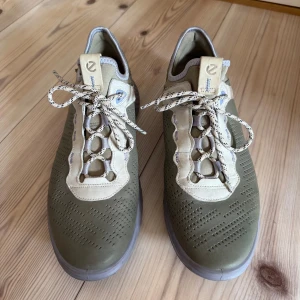 Gröna sneakers från ECCO strl 41 - Snygga gröna sneakers från ECCO med beige och ljusgrå detaljer. Skorna har perforerat mönster på ovansidan, rund tå och platt sula. coola kontrastfärgade skosnören. Perfekt för dig som gillar stilren och sportig look. Skorna är endast andvända ett par gånger. De får inte plats hemma längre och därför säljer jag dem till ett bra pris.