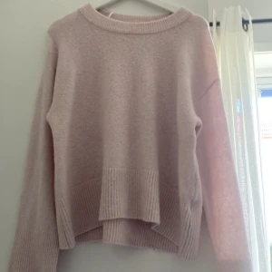Ljusrosa stickad tröja Gina Tricot - Supermysig ljusrosa stickad tröja från Gina Tricot med bred ribbad kant vid nederdelen och ärmsluten. Tröjan har en loose passform och långa ärmar, perfekt för chilliga dagar. Enkel design med rund hals och mjukt material.