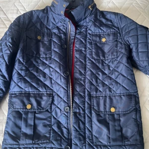 Quiltad blå jacka Tommy Hilfiger Xs - Snygg quiltad blå jacka från Tommy Hilfiger i storlek XL i barnstorlek. Den är som xs och passar bra om du är 170cm. Jackan har fyra fickor med lock och guldiga knappar, hög krage och dragkedja samt knappar framtill. Perfekt för dig som vill ha en stilren och klassisk look med extra detaljer.