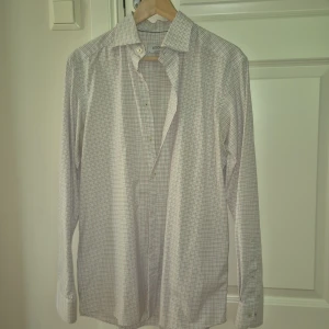 Rutig vit skjorta från Eton, M - Snygg vit skjorta från Eton i storlek M med rutigt mönster i blått och rött. Skjortan har klassisk krage, långa ärmar med dubbla knappar vid manschetten och är tillverkad i mjuk bomull. Perfekt för dig som gillar stilrena detaljer och tidlös design.