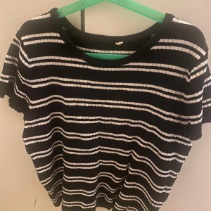 Svartvit randig ribbad topp - Svart ribbad topp med vita horisontella ränder och korta ärmar. T-shirten har rund halsringning och en lätt vågig kant nertill. Perfekt för en chill och stilren look.