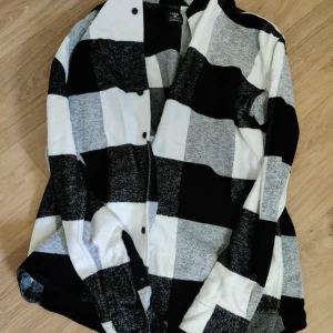 Svartvit rutig overshirt - Snygg overshirt från Stradivarius i svartvitt rutigt mönster. Skjortan har knappar framtill och är långärmad. Perfekt att slänga över en t-shirt för en avslappnad look.