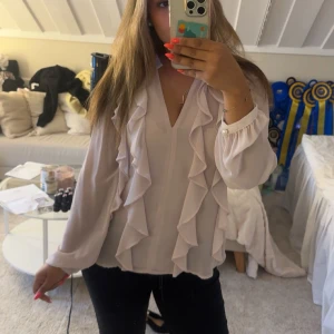 Ljusrosa blus med volangdetaljer - Supersöt ljusrosa blus från Zara med v-ringning och volanger längs framstycket. Långa ärmar med pärlknapp vid mudden. Helt oanvänd. Storlek S💕 
