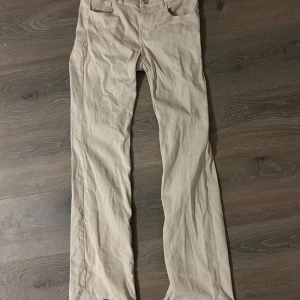 Beiga lågmidjade raka jeans från H&M Divided - Snygga beiga byxor från H&M Divided i rak modell. Byxorna har klassisk femficksdesign, bälteshällor och stängs med knapp och dragkedja. Tillverkade i bomull med lite stretch för extra komfort. Perfekta till en avslappnad stil. Inte så mycket använda