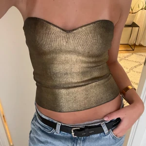 Guldig bandeau tubtopp - Säljer en guldig bandeau tubtopp med snygg sweetheart-urringning. Toppen är figurnära och axelbandslös, perfekt för att sticka ut. Materialet är glansigt och ger en lyxig känsla. 🩷🩷🩷 Skriv för fler bilder!!