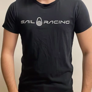 Svart Sail Racing t-shirt med tryck - Svart t-shirt från Sail Racing i storlek S med stilrent vitt logotryck över bröstet och en mindre logga i nacken. Klassisk rund hals och korta ärmar. Materialet känns mjukt och lätt, perfekt för en chill look.