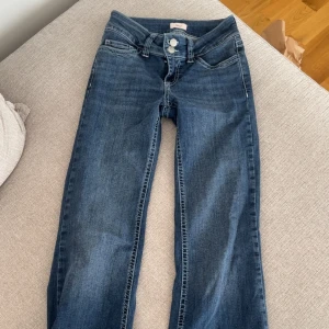 Blå jeans från Nelly med broderade fickor - Snygga blå jeans från Nelly med raka ben och klassisk femficksmodell. Baksidan har coola broderade detaljer på fickorna i vitt. Jeansen har dubbla silverfärgade knappar och är tillverkade i mjukt denimtyg. Perfekta för en avslappnad och trendig look. DOM ÄR UPPSYDDA SÅ DE PASSAR MIG SOM ÄR 156/157 CM LÅNG! Går nog att sprätta upp! Säljer då jag vill köpa en annan färg.