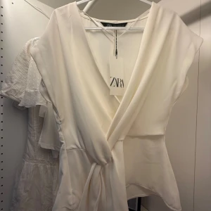 Vit omlottopp från Zara - Säljer en snygg vit omlottopp från Zara med knyt i midjan. Helt ny med prislapp. Orginalpris 329 och säljer för 299