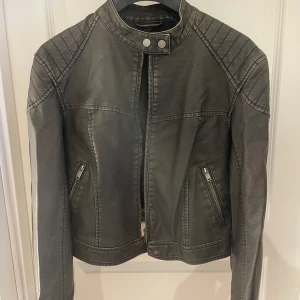 Brun svart bikerjacka från Gina Tricot S - Snygg brun svart bikerjacka från Gina Tricot i storlek S. Jackan har coola quiltade detaljer på axlarna, dragkedjor vid fickorna och framtill samt en hög krage med tryckknappar. Materialet är syntet som ger en skinnliknande känsla. Perfekt för en edgy look.