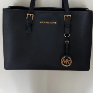 Svart handväska från Michael Kors - Stilren svart handväska från Michael Kors med guldfärgade detaljer och MK-logga. Väskan har rektangulär form, flera fack med dragkedja och innerfoder med MK-mönster. Tillverkad i skinn med justerbara handtag och snyggt hängande MK-emblem. Den är precis som ny då jag använt den 2-3 gånger och därefter så har den stått i min garderob!! Ni ser ju skicket både utsida och insida! Men den har en liten fläck på baksidan that’s it!!💞Kommer i tillhörande mk påse!Vid snabb affär kan jag tänkas sänka pris!