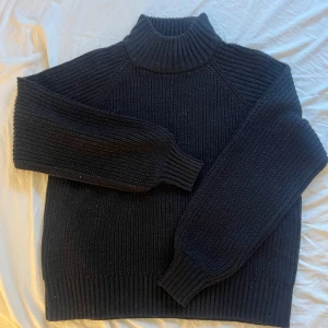 Svart stickad polotröja från Vero Moda  - Mysig svart stickad polotröja från Noisy May med grov ribbstickning och hög krage. Tröjan har lång ärm och en relaxed fit som är perfekt för kyliga dagar. Enkel att matcha med jeans eller kjol för en chill look.