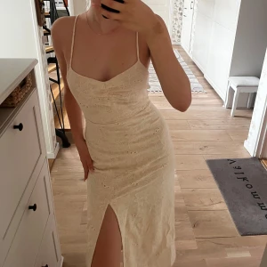 Beige blommig klänning från Mango - Superfin beige klänning från Mango med broderade blommor, smala axelband och slits framtill. Klänningen är figurnära och har en v-ringad urringning samt öppen rygg. Perfekt för sommarens alla tillfällen! Är helt ny, men passar tyvvär inte! 