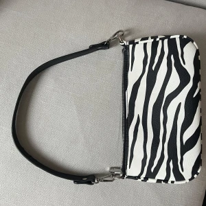 Zebramönstrad axelväska - Säljer en snygg axelväska från Gina Tricot med zebramönster i svart och vitt. Väskan har ett avtagbart axelband och stängs med dragkedja. Använd ett fåtal gånger därav superfint skick! Nypris 600!