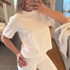 Vit t-shirt med dragsko - Säljer en basic vit t-shirt med rund hals och korta ärmar. T-shirten har en avslappnad passform. Perfekt till vardags och enkel att matcha med allt.