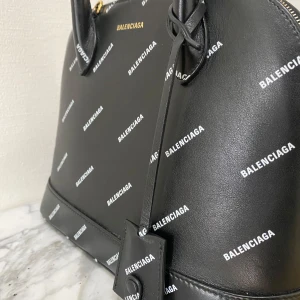 Svart handväska från Balenciaga - Unik handväska från Balenciaga med vitt logomönster över hela väskan. Väskan har rundad form, dubbla handtag och dragkedja upptill. Avtagbar axelrem medföljer. Guldiga metalldetaljer och en liten tag framtill. Perfekt för dig som gillar lyxiga accessoarer. Köptes för ca 21000kr, säljes till vrakpris. Kvitto finns ej. Bredd ca 27 cm, höjd ca 21 cm. Pyttesmå slittecken på botten av väskan. Säljes i befintligt skick. Garanterat äkta!