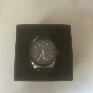 Svart klocka från Tommy Hilfiger - Stilren klocka från Tommy Hilfiger med mörkblå  urtavla och silverfärgat armband i metall. Låda, kvitto och extra längd tillkommer.