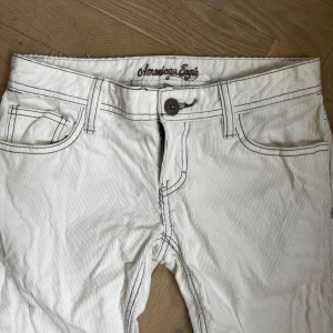 Vita manchester jeans från American Eagle - Säljer ett par vita manchester från American Eagle. Jag är 169 cm lång, innerbenet är ca 32,5 cm och midjan är ca 12,5 cm bred. De är för små i midjan på mig men bra i längden. Skulle säga att de passar perfekt för en 32. 