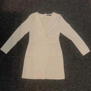Vit kavajklänning från Boohoo - Säljer en stilren vit kavajklänning från Boohoo med lång ärm och klassisk krage. Klänningen har figurnära passform och dragkedja i ryggen. Perfekt för dig som gillar en chic och modern look. Aldrig använd.
