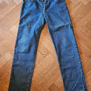 Blå jeans från Marlboro Classics - Klassiska blå jeans från Marlboro Classics med raka ben och normal passform. Jeansen har knappar i gylfen och tydliga sömmar. Märkespatch bak i midjan och klassiska bakfickor. Perfekta för en avslappnad stil.