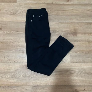 Svarta raka jeansbyxor - Säljer ett par svarta jeansbyxor med klassisk femficksdesign och raka ben. Byxorna har normal passform och stängs med dragkedja och knapp. Perfekta till många olika outfits och enkla att matcha.