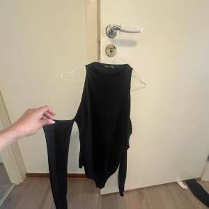 Svart oneshoulder bodysuit från Nelly - Säljer en svart oneshoulder bodysuit från Nelly. Toppen har en ärm och en axel är bar, vilket ger en trendig look. Perfekt att styla med jeans eller kjol för en cool outfit.