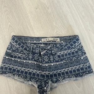Mönstrade blå-vita shorts från Denim Co. - Säljer ett par blå-vita shorts från Denim Co. med etniskt inspirerat mönster och råa fransiga kanter. Shortsen har normal passform och klassisk femficksdesign. Perfekta för sommardagar och festivaler!