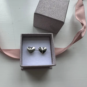 Hjärt studs i silver - Säljer ett par silvriga hjärt studs som tyvärr aldrig kommit till användning. De kommer i en glittrig ask med rosa band. 