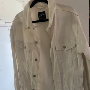 Vit jeansjacka från Zara - Säljer en stilren vit jeansjacka från Zara. Klassisk modell med bröstfickor med lock och knappar framtill. Perfekt att slänga över en t-shirt eller hoodie för en fräsch look.