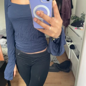 Mörkblå långärmad topp med vid ärm - Säljer en mörkblå långärmad topp med bred, fyrkantig ringning och vida ärmslut. Modellen är tight och croppad, perfekt att styla med höga byxor. Materialet känns mjukt och stretchigt.
