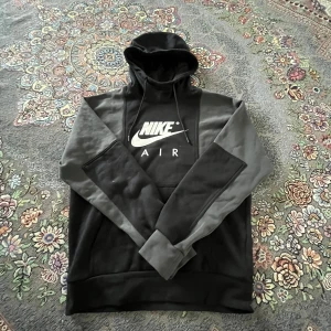 Svart och grå Nike Air hoodie - Säljer en svart och grå hoodie från Nike Air med vit logga framtill och texten 'GET OVER YOUR FEAR OF HEIGHTS' på ryggen. Tröjan har huva och långa ärmar, perfekt för en sportig och avslappnad stil.