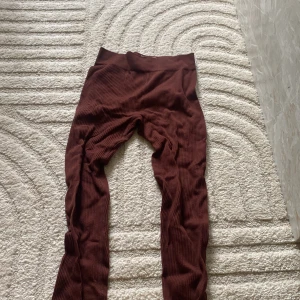 Bruna ribbade leggings från PrettyLittleThing - Säljer ett par bruna ribbade leggings från PrettyLittleThing. De är stretchiga och har hög midja, perfekta för en bekväm och snygg look. Materialet är mjukt och följsamt med 92% polyamid och 8% elastan.