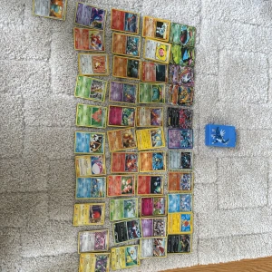 Samling Pokémonkort med kortlåda - Stor samling Pokémonkort i olika färger och motiv, inklusive flera holografiska och EX-kort. Blandade generationer och typer, med en blå kortlåda med motiv. Perfekt för samlare eller spelare som vill utöka sin samling. Man får allihopa i köpet, flera kort är från tidigt 2000-talet och 1990-talet.