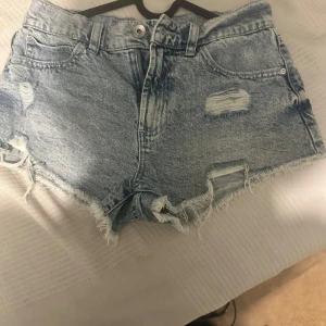 Ljusblå slitna jeansshorts -  Det är gratis frakt om man swishar direkt till mig. Då betalr man bara priset Säljer ett par ljusblå jeansshorts med slitna detaljer och fransig kant. Shortsen har klassisk femficksdesign och knappgylf. Perfekta för varma dagar och en avslappnad stil.