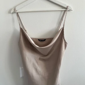 Beige satinlinne med smala axelband - Säljer en stilren beige satinlinne från shein med smala axelband och snygg draperad urringning. Perfekt för dig som gillar minimalistisk och elegant stil. Linnet har en mjuk glans och följsam passform.