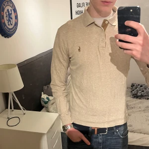 Beige pikétröja från Ralph Lauren - Säljer en stilren beige långärmad pikétröja från Ralph Lauren med klassisk krage och knappar framtill. Tröjan har den ikoniska broderade loggan på bröstet och är tillverkad i mjukt material. Perfekt för en avslappnad men snygg look. Rugbytröja. Jag är 186 cm lång. Står M i tröjan men sitter mer som S