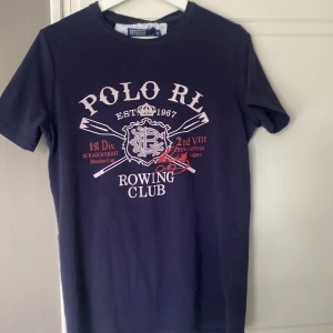 t-shirt från Polo Ralph Lauren - t-shirt från Polo Ralph Lauren med tryck framtill som säger 'Polo RL Rowing Club'. Klassisk passform och korta ärmar. Perfekt för en sportig och avslappnad stil. Säljer då den inte passar mig, perfekt nu till sommaren! Pris går att diskutera 