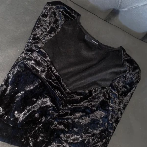 Svart sammetsblus från Vero Moda - Supersnygg svart sammetsblus från Vero Moda med lång ärm och figurnära passform. Blusen har en unik struktur i tyget som ger en lyxig känsla och en snygg urringning. Perfekt för dig som vill sticka ut lite extra. HAR ENDAST ANVÄNT EN GÅNG