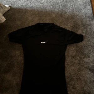 Svart Nike Pro Dri-FIT t-shirt - Säljer en svart Nike Pro Dri-FIT t-shirt med klassisk vit Nike-logga på bröstet. T-shirten är kortärmad och tillverkad i ett skönt material som tar upp svett. Den är liten i storleken så om man har M passar den suveränt
